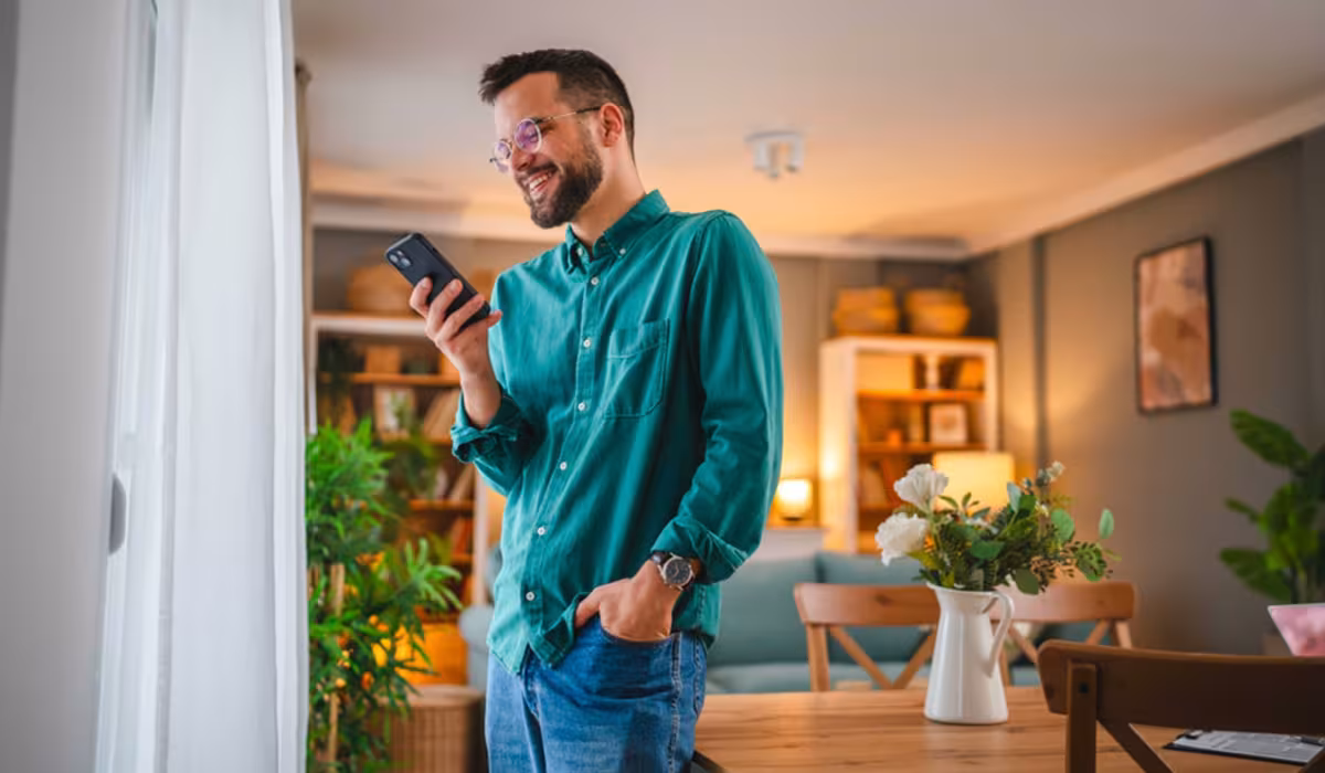 Uomo sorridente che guarda lo smartphone in un soggiorno luminoso