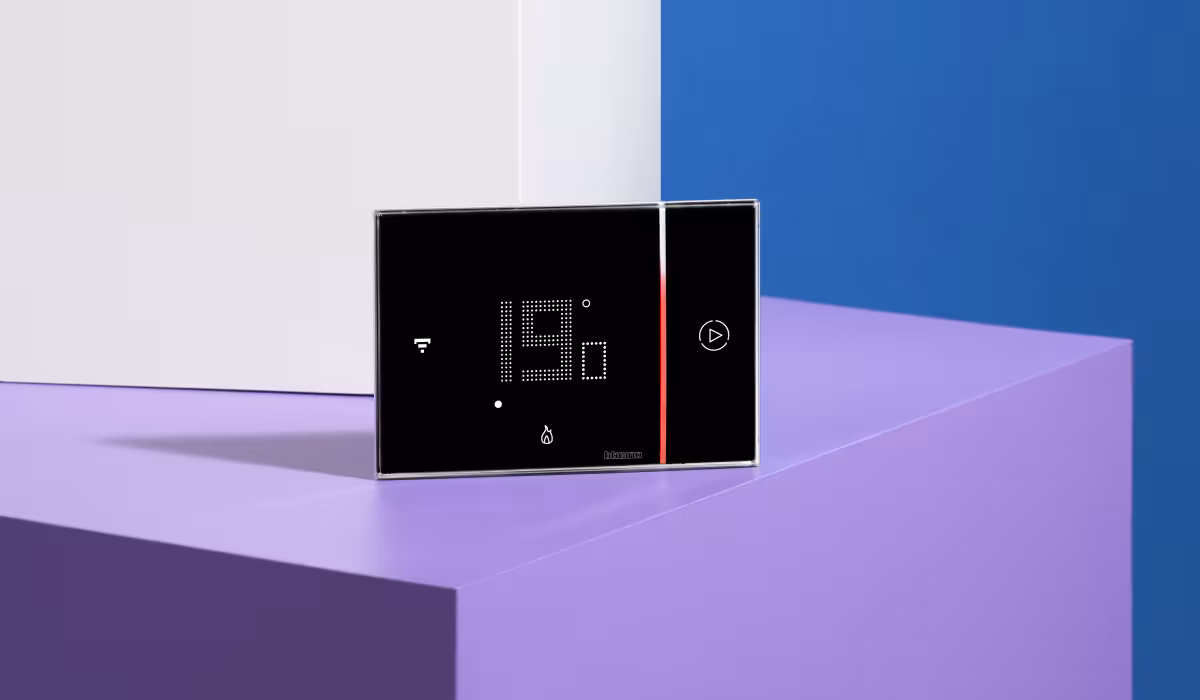 Termostato Smarther2 with Netatmo con display acceso a 19°, appoggiato su piedistallo viola con sfondo bianco e blu