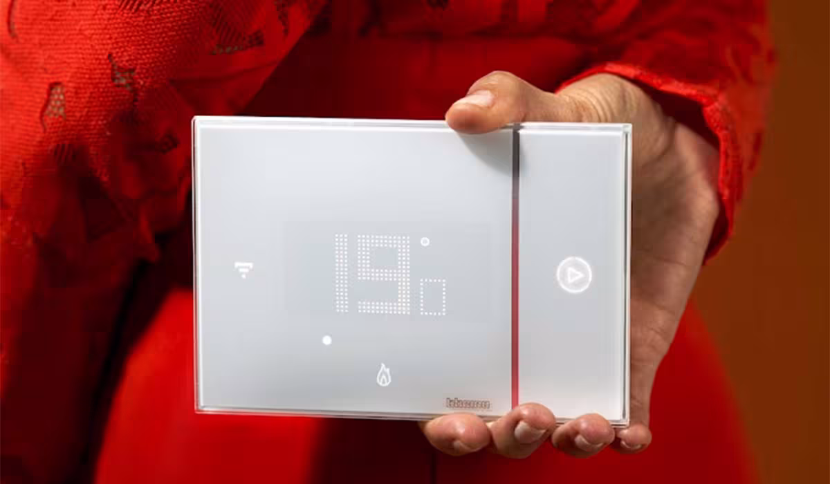 Donna con abito rosso che tiene in mano il termostato Smarther2 bianco di BTicino