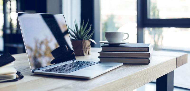 Postazione di lavoro in soggiorno con tavolo in legno, laptop, libri e una tazza di caffè