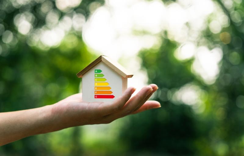 Mano che sostiene una casa con scala di efficienza energetica al suo interno