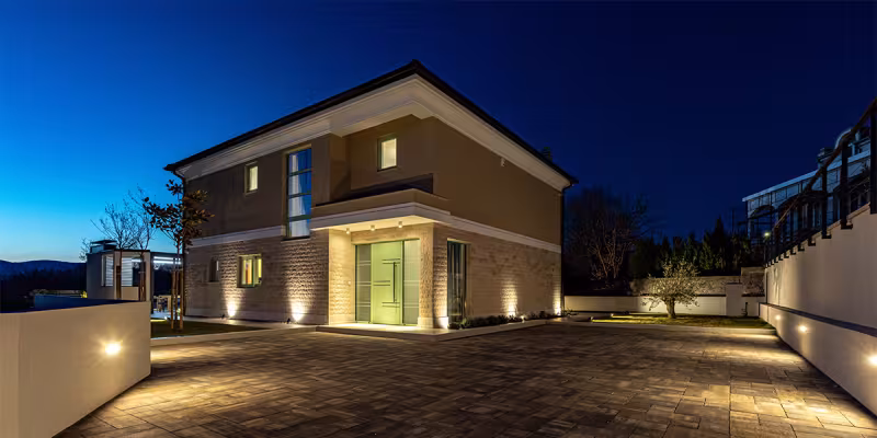 Villa moderna a due piani illuminata, con cortile pavimentato, fotografata al crepuscolo