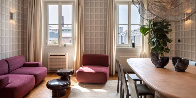 Soggiorno moderno luminoso Archiproducts con divano rosso, tavolo in legno, sedie nere e grandi finestre