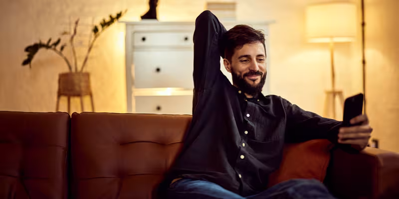 Uomo rilassato sul divano che controlla lo smartphone in un soggiorno moderno con luci soffuse