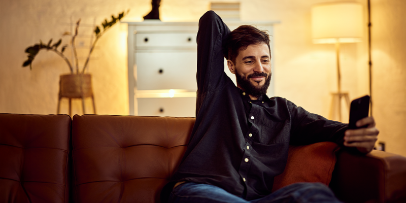 Uomo rilassato sul divano che controlla lo smartphone in un soggiorno moderno con luci soffuse