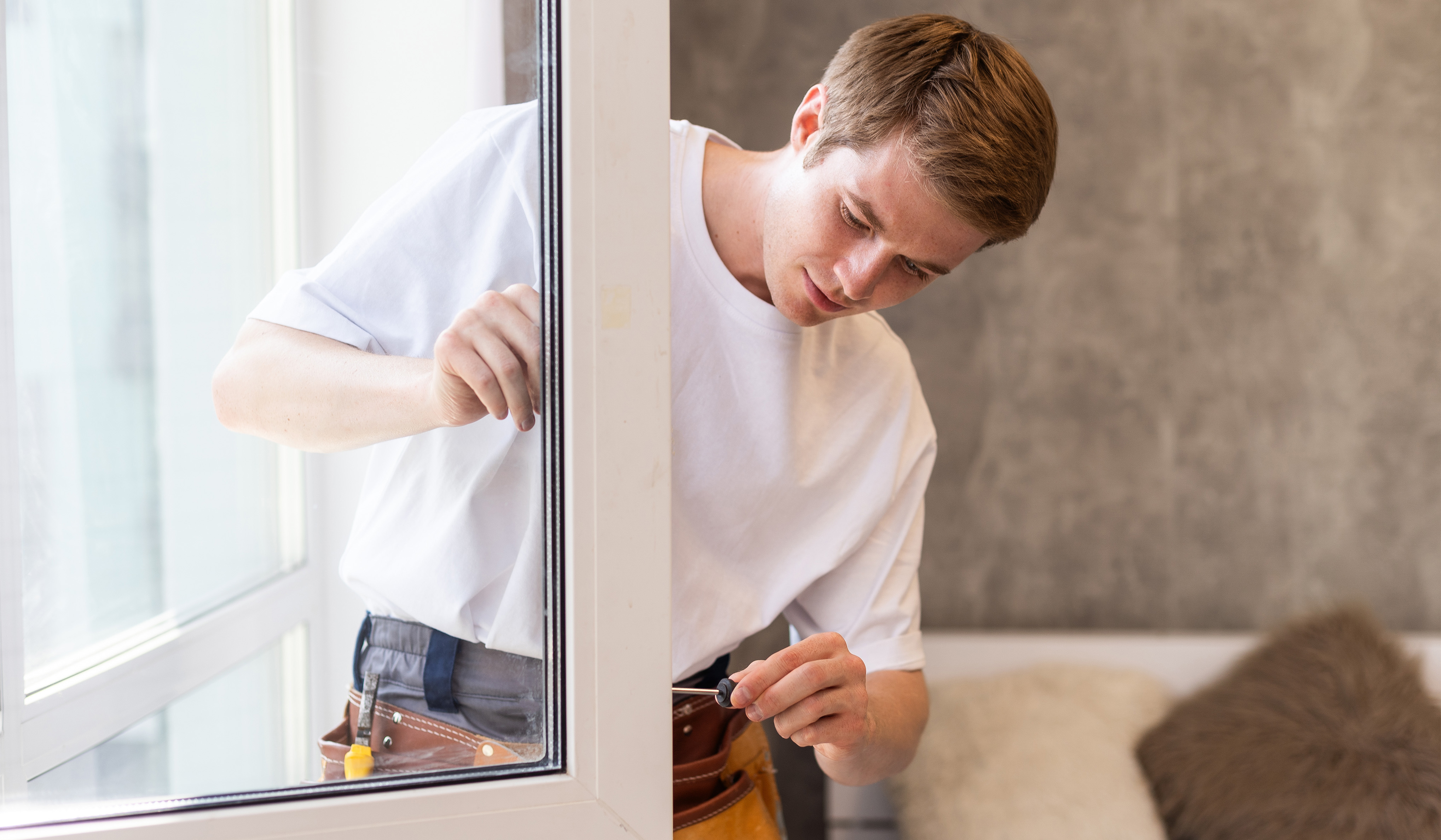 Tecnico in maglietta bianca con cintura porta utensili durante il montaggio di una finestra in una casa luminosa