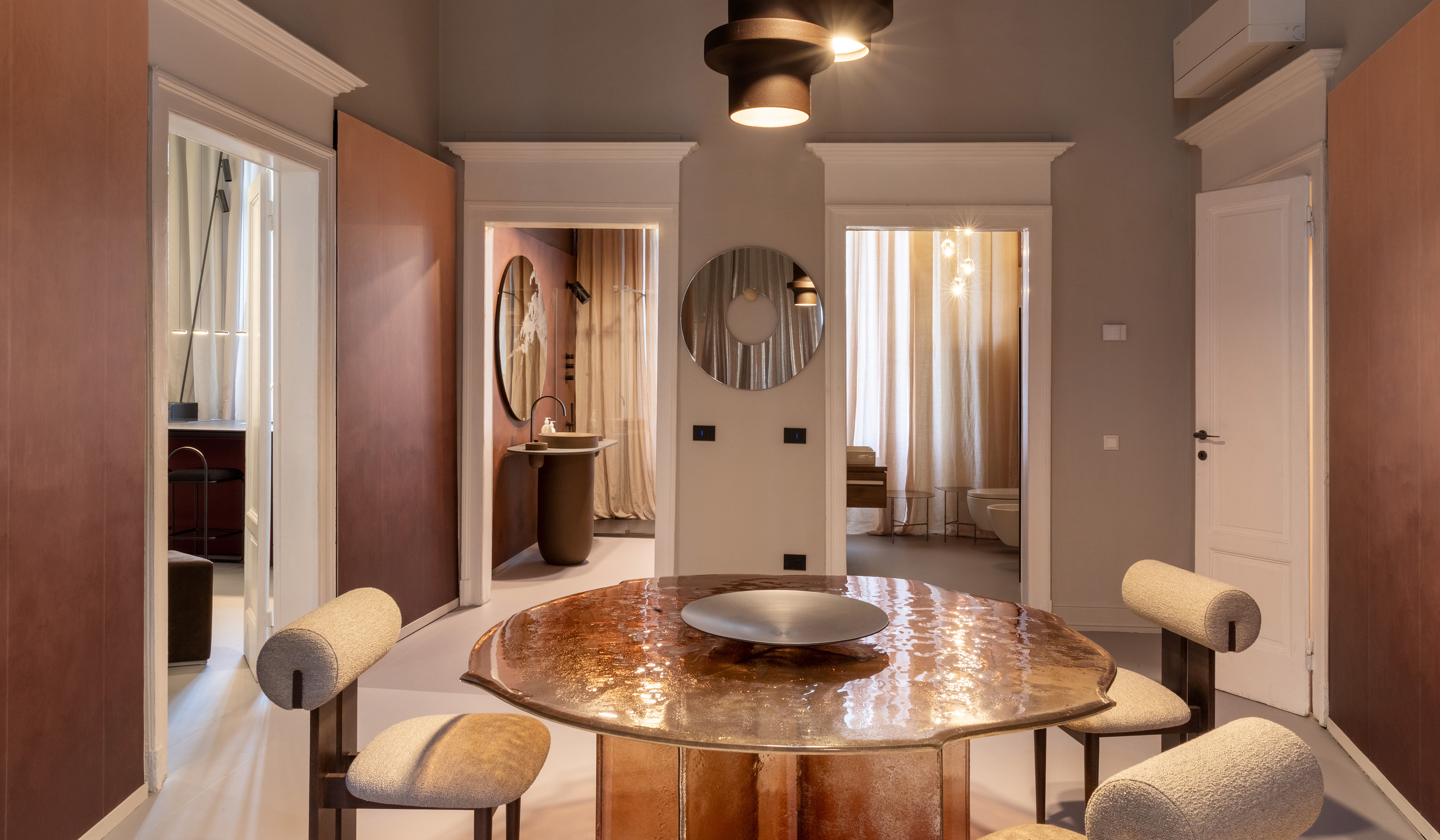 Sala da pranzo moderna Archiproducts con tavolo rotondo, sedie imbottite, lampade a sospensione e porte verso altre stanze